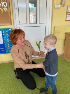 Chłopiec trzyma wicuągiętą rękę z tulipanem w stronę Pani, która kuca.