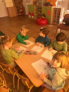 Pięcioro dzieci siedzących przy stoliku i kolorujących kolorowanki.