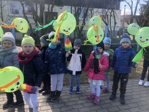 Grupa dzieci idąca na spacer i trzymająca w rękach zielone, ozdobione balony.