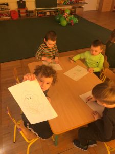 Czworo dzieci siedzących przy stoliku i kolorujących kolorowanki.