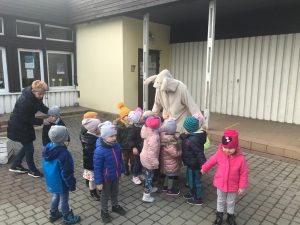 Grupa dzieci będąca w ogrodzie przedszkolnym. Za dziećmi stoją dwie Panie. Pani po prawej stronie ma na sobie ubrany strój zajączka.