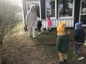 Czworo dzieci będących w ogrodzie przedszkolnym wraz z Panią przebrana za zajączka. Troje dzieci gtrzyma w rękach koszyczki wielkanocne.