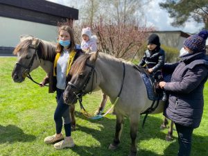 Chłopiec i dziewczynka siedza na koniu. Po środku i obok chłopca stoją Panie.