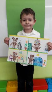 Uśmiechnięty chłopiec stoi trzymając z rękach rysunek z misiami.
