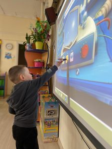 Chłopiec trzymający w ręku interaktywny pisak i wykonujący zadanie na tablicy multimedialnej