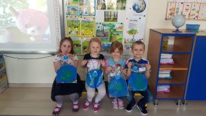 Czworo dzieci trzymajacych w rękach prace plastyczne planetę Ziemię.
