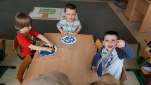 Troje dzieci siedzących przy stoliku i wykonujących prace plastyczne - planetę Ziemię.