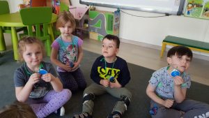 Czworo dzieci siedzących na dywanie w sali przedszkolnej i pokazujących zawieszone na szyi medale.