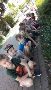 Dzieci kucają wzdłuż chodnika. Obok posadzone są niezapominajki.