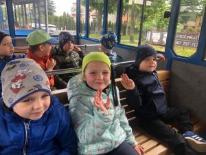 Siedmioro dzieci siedzących w kolejce turystycznej na dwóch ławkach.