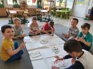 Siedmioro dzieci wykonujących pracę plastyczną. Czworo dzieci ma umoczony w farbie palec i wykonuje kropki na serwetkach.