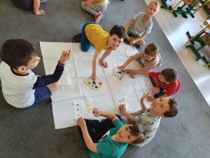 Siedmioro dzieci wykonujących pracę plastyczną. Sześcioro dzieci ma umoczony w farbie palec i wykonuje kropki na serwetkach.