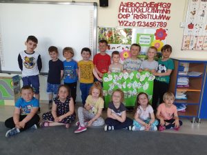Grupa dzieci pozująca do zdjęcia grupowego w dwóch rzędach. Dzieci stojący w drugim rzędzie trzymają w rękach pracę plastyczną.