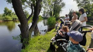 Grupa dzieci na wózkach i Pań patrza na staw i kaczki.