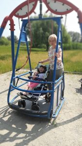 Dziewczynka na wózku obok Pani huśtają się na huśtawce.