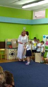3 chłopców stoi w jednym rzędzie. Obok nich stoi Pani Dyrektor i wręca dziewczynce torbę z prezentem.