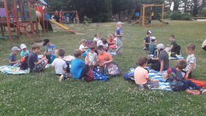 Duża grupa dzieci siedzi na kocach na trawie