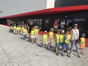 Grupa dzieci idących wraz z trzema paniami po placu ostrowskiej Areny. Chłopiec w ostatnim rzędzie jedzie w wózku.