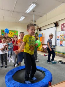 Chłopiec skacze na trampolinie, za nim grupa dzieci.