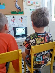 2 chłopców siedzi na krześle. Oglądają bajke na laptopie