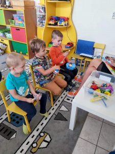 Chłopcy siedza na krześle. W rękach trzymają instrumenty.