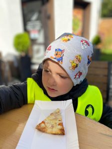 Chłopiec jedzący kawałek pizzy.