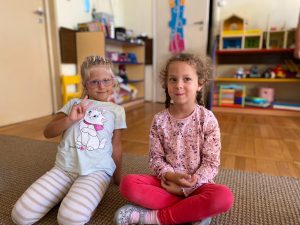 Dwie dziewczynki siedzące na dywanie w sali przedszkolnej.