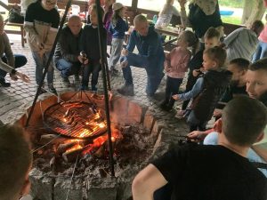 Mężczyźni i kobiety smażący kiełbaski przy ognisku.