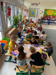 Grupa dzieci siedzi przy stolikach i kolorują obrazek.