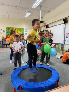 Chłopiec skacze na trampolinie, za nim grupa dzieci.