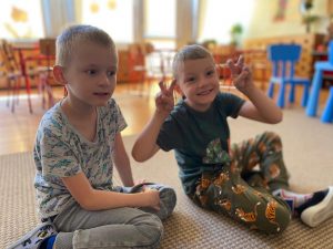 Dwóch chłopców siedzących na dywanie w sali przedszkolnej.