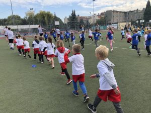 Dzieci ustawione w rzędach, biegające po boisku sportowym.