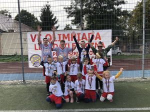 Dziesięcioro dzieci pozujących do zdjęcia w dwóch rzędach. Za dziećmi stoją dwie nauczycielki i dwóch chłopaków. Wszyscy trzymają ręce podniesione do góry.