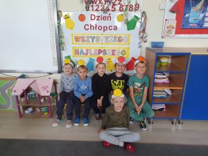 Pięcioro chłopców siedzących na ławce w sali przedszkolnej. Przed dziećmi siedzi chłopiec po turecku. Wszyscy chłopcy mają na głowach opaski.