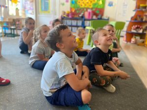 Siedmioro dzieci siedzących w sali przedszkolnej na dywanie.