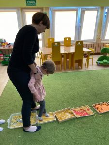 Dziewczynka trzymana za rękę przez Panią chodzi po pojemnikach z makaronem.