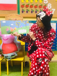 Nauczycielka w przebraniu myszki Minnie trzyma w rękach książkę, którą czyta dzieciom.