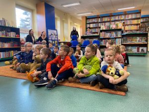 Duża grupa dzieci siedzi na dywanie w bibliotece.