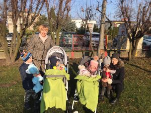 2 dzieci na wózkach, 2 dzieci stoi i 2 Panie na dworze. Dzieci trzymają w rękach pluszaki.