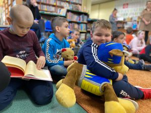 Duża grupa dzieci siedzi na dywanie w bibliotece.