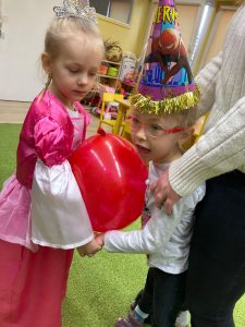 Dziewczynki trzymając się za ręce tańczą z balonem przy brzuchu.
