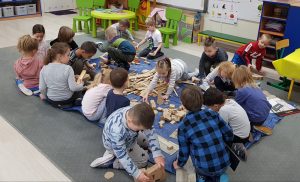 Grupa dzieci wybiera kawałki drewna do wykonania swojej pracy. Drewno położone jest na granatowej płachcie.