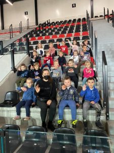 Na trybunach hali sportowej siedzą dzieci i machają.