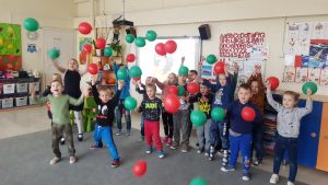 duża grupa dzieci stoi na dywanie w przedszkolnej sali . Dzieci podrzucają kolorowe balony.