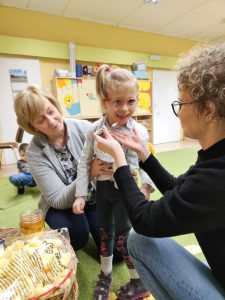 Dziewczynka próbuje miód na łyżeczce, który podaje jej mauczycielka.