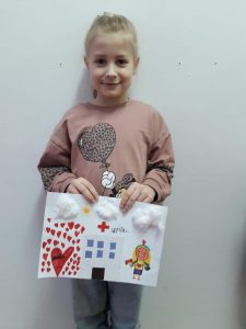 Dziewczynka trzyma w ręce wykonaną pracę plastyczną.