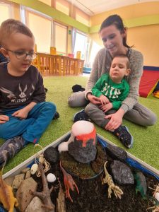 2 chłopców i Pani siedzą obok makiety wulkanu.