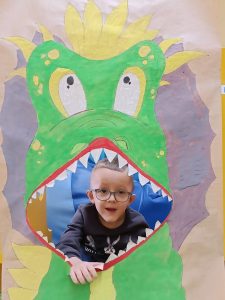 Chłopiec siedzi na plakatem przedstawiającym dinozaura z otwartą buzią.