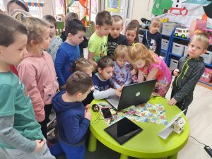 Dzieci ustawione przy zielonym stoliku, na którym znajduje się laptop.