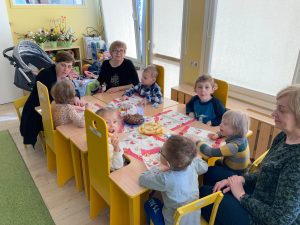 Dzieci siedzą przy stolikach i jedzą słodki poczęstunek z okazji dnia kobiet.